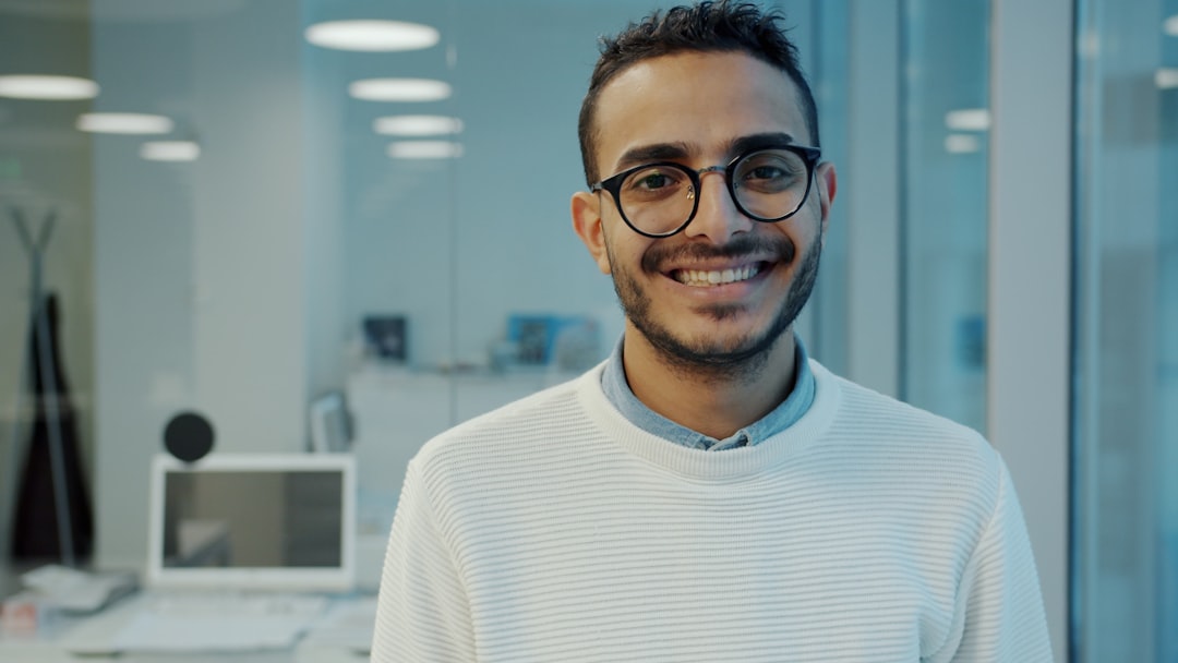 A smiling man wearing glasses in an office setting. - Photo by Vitaly Gariev on Unsplash
